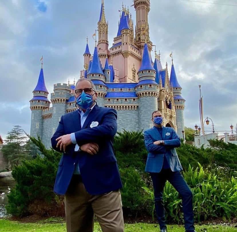Guests wearing masks enjoy the festivities in front of Cinderella Castle at Walt Disney World, with a dramatic cloudy sky setting the scene for the park’s 50th Anniversary Celebration.