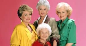 The beloved cast of The Golden Girls beams in vibrant, themed outfits against a playful pink backdrop, celebrating their timeless comedy as the show streams on Disney+.