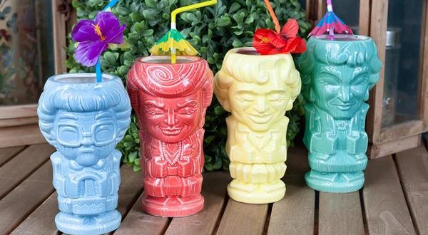 A set of four vibrant Geeki Tikis mugs themed after The Golden Girls, each topped with fun straws and decorative accents, displayed on a wooden table surrounded by lush greenery—an eye-catching collectible for fans gearing up for a Disney+ binge or bringing theme park flair to their at-home entertainment.