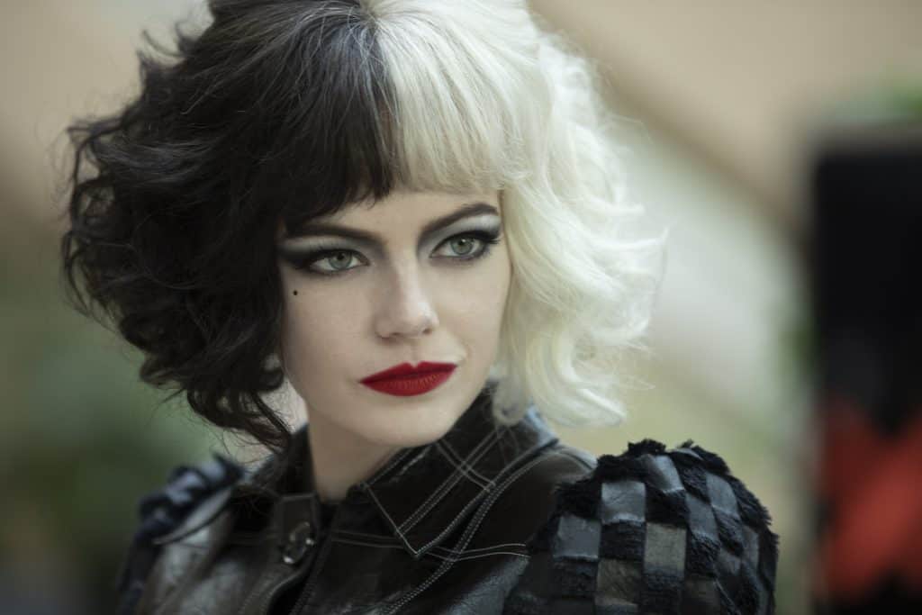 Cruella De Vil, with her signature black and white hair, dramatic makeup, and bold checkered jacket, glances to the side in a look straight from the first Cruella movie trailer—a striking representation of her rebellious Disney Villains style perfect for character meet-and-greets or themed entertainment events.