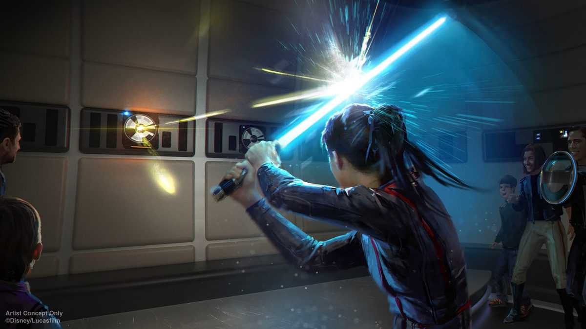 A Star Wars: Galactic Starcruiser guest wields a blue lightsaber to deflect laser blasts during an interactive onboard experience, as fellow travelers look on in excitement.