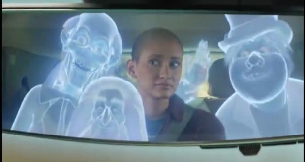 The Chevy Bolt EUV glides through the scene as three glowing blue Hitchhiking Ghosts from the Haunted Mansion materialize around it, capturing a moment where Disney magic meets modern innovation.