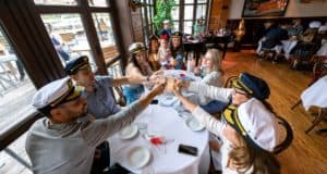 A lively group at The Boathouse in Disney Springs, all wearing captain hats, raise their glasses for a toast around the table during the energetic Sing Along Brunch, soaking up the sunshine and festive Disney atmosphere.