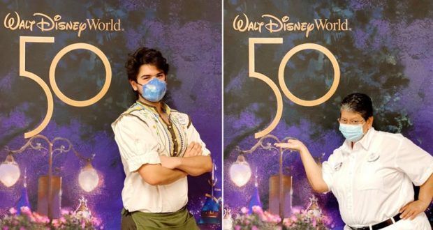 Disney Cast Members sporting masks strike a fun pose in front of the shimmering Walt Disney World 50th Anniversary celebration backdrop.