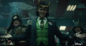 Loki, dressed in his iconic green suit and horned helmet, welcomes fans with a mischievous grin and open arms as two stern guards stand by—setting the stage for his latest Disney+ adventure.