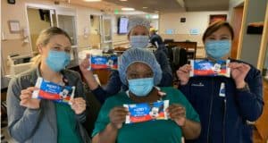 Four healthcare workers wearing masks at AdventHealth Orlando happily hold up Mickey Ice Cream Bars inside a hospital, marking the magical collaboration between Disney and the hospital as official Health Partners.
