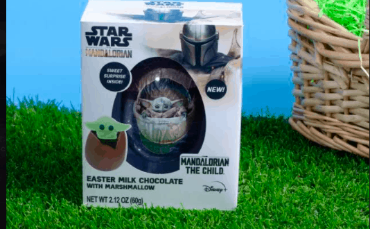 Mandalorian Easter milk chocolate box from the Star Wars universe, showcasing a charming Chocolate Egg and Baby Yoda (Grogu) relaxing on green grass with a vibrant blue backdrop, perfect for fans at Galaxy’s Edge or any themed entertainment venue.