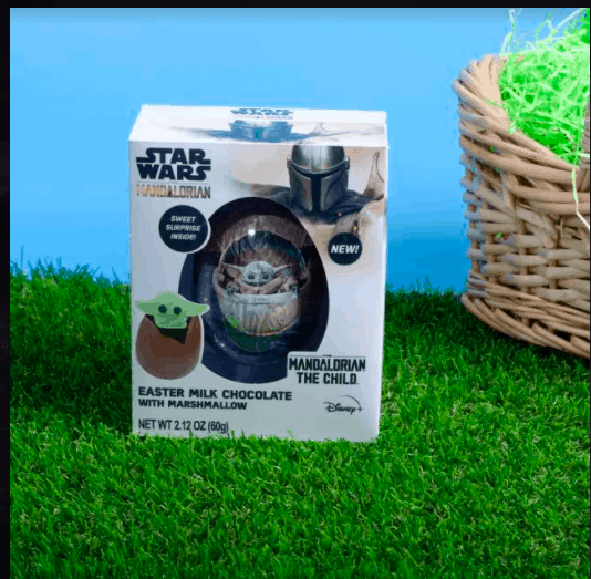 Mandalorian Easter milk chocolate box from the Star Wars universe, showcasing a charming Chocolate Egg and Baby Yoda (Grogu) relaxing on green grass with a vibrant blue backdrop, perfect for fans at Galaxy’s Edge or any themed entertainment venue.