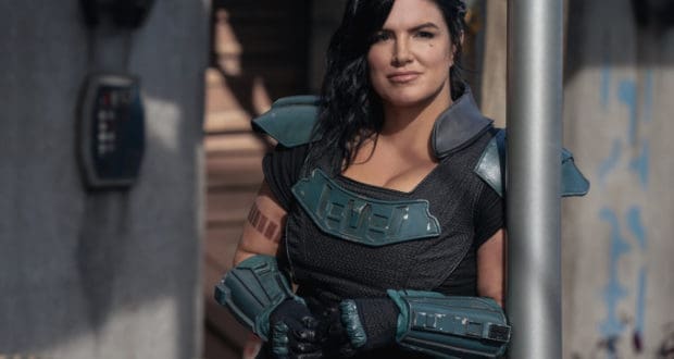 A futuristic heroine, channeling Gina Carano’s bold energy, stands outside on the grounds of an epic adventure park. With arms crossed and a confident expression, she strikes a powerful pose as if ready to lead guests on the next thrilling attraction.