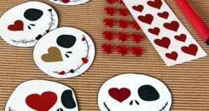 Five Jack Skellington-inspired skull crafts decorated with hearts and stickers, accompanied by a red marker on a rustic table, channel the spooky-sweet spirit of Halloween Town for the ultimate Disney-themed Valentine’s Day activity.