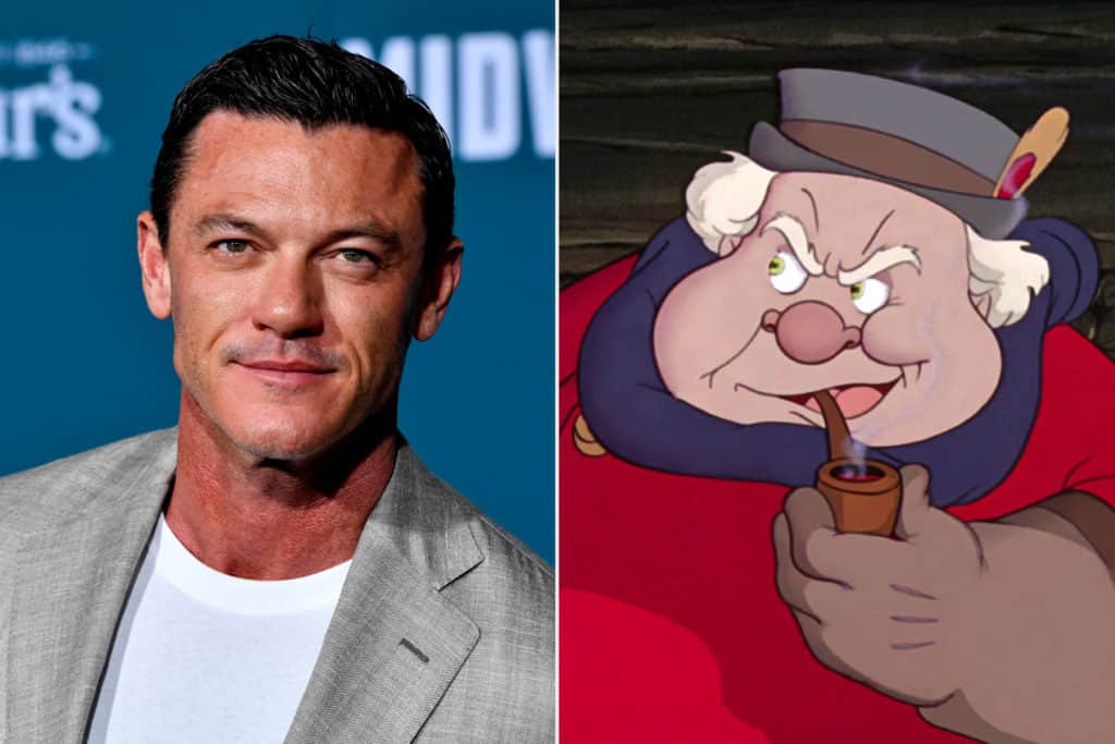 Luke Evans, dressed in a sharp gray suit and smiling, stands beside an animated Pinocchio sporting his signature hat and pipe. Both are set against vibrant blue and dark backgrounds in a scene that brings the magic of Disney’s Live-Action Pinocchio to life, echoing the theatrical charm Evans displayed as Gaston in Beauty and the Beast—a treat for fans of Disney’s immersive entertainment experiences.