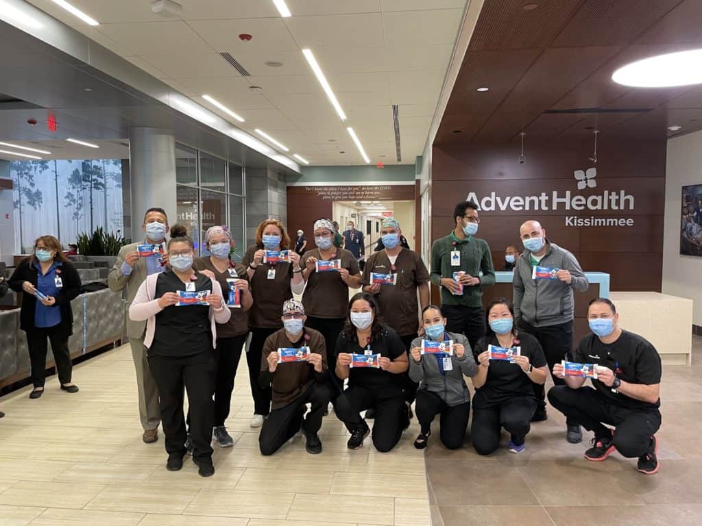 Healthcare heroes at AdventHealth Kissimmee hospital lobby wear masks and raise cards in support of Disney’s Health Partner, proudly celebrating their collaboration with the Disney family.