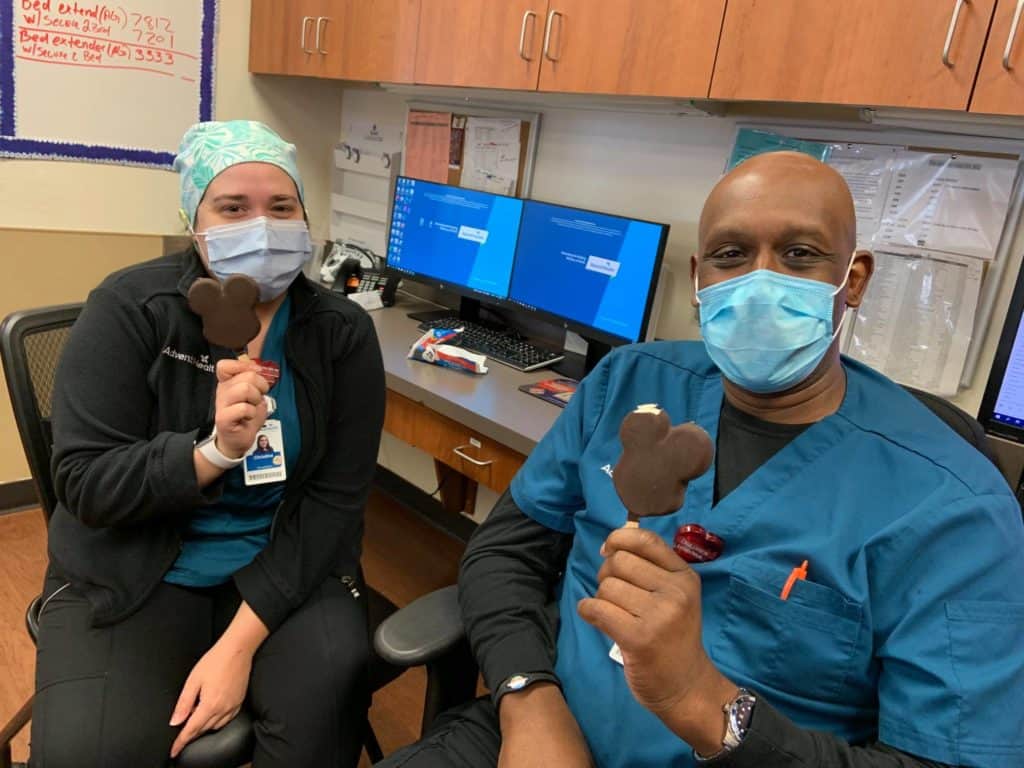Disney magic comes to the workplace as two healthcare heroes in scrubs and masks enjoy iconic Mickey Mouse-shaped ice cream bars, celebrating a collaboration between Disney Health Partner and AdventHealth Orlando right in their office.