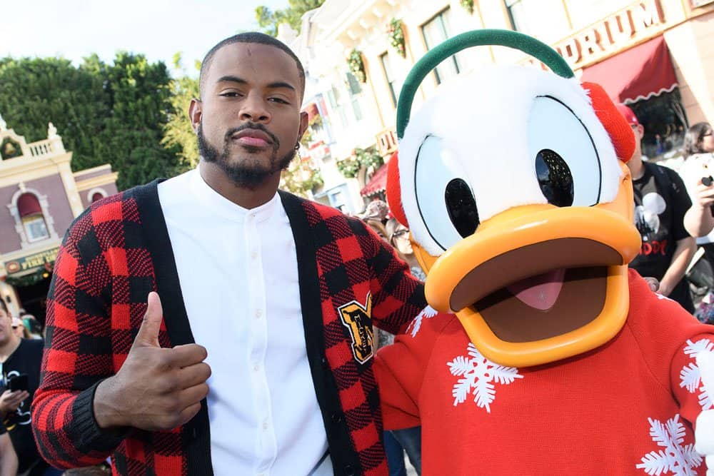 A guest in a trendy plaid sweater flashes a thumbs up beside Donald Duck, who’s sporting a festive holiday pullover, at a lively Disney Parks holiday event. The celebration radiates the cool energy of a grown-ish episode, dripping with style that fans like Trevor Jackson would love.