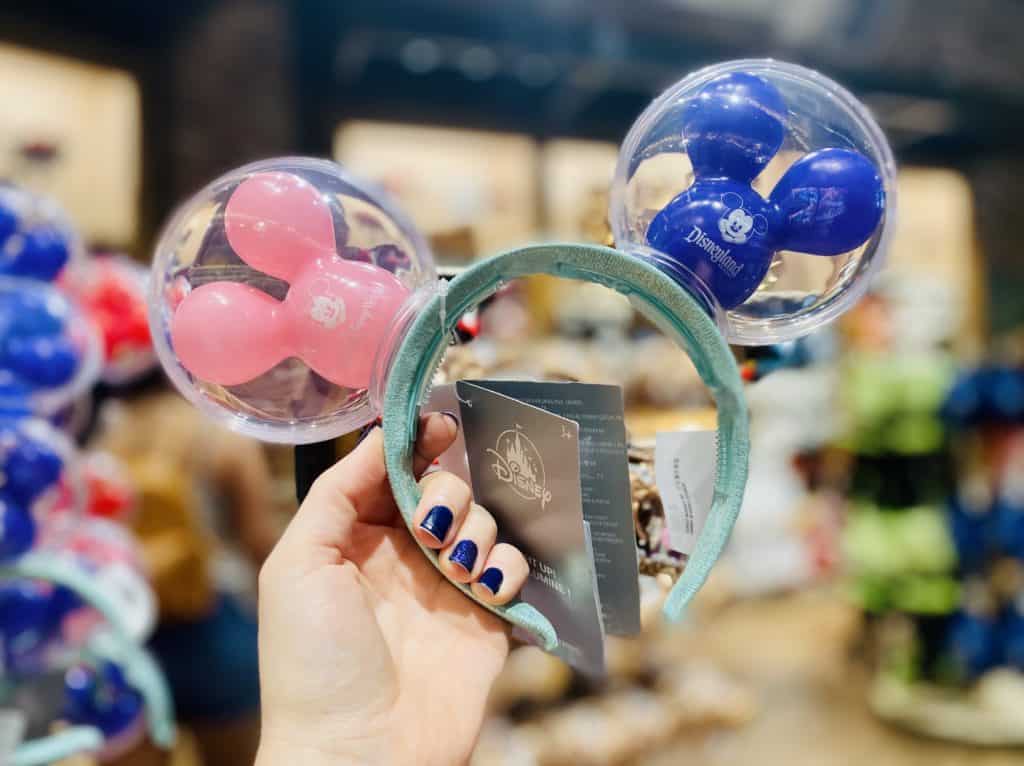 Disney fan showing off a whimsical headband from Disney Springs, featuring clear pastel balloon ears with pink and blue Mickey Mouse balloons nestled inside—an absolute must-have accessory for your next park adventure.