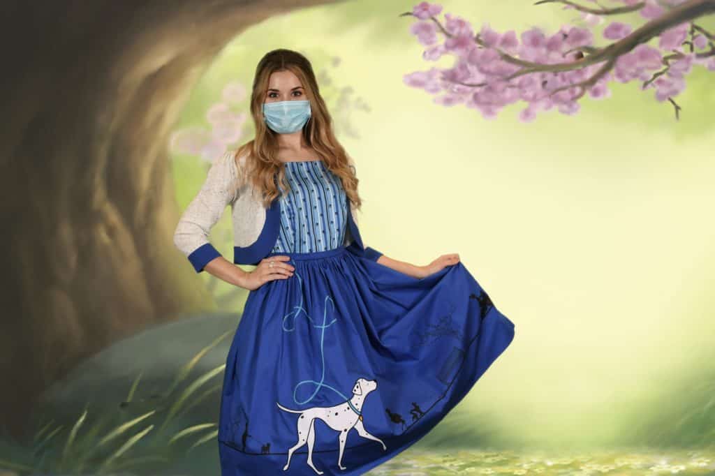 A Disney fan dressed in a playful 101 Dalmatians-inspired dress with an adorable dog pattern and a protective mask, posing against a dreamy pastel forest scene—the perfect ensemble for exploring Disney Springs or enjoying any whimsical day at the park.