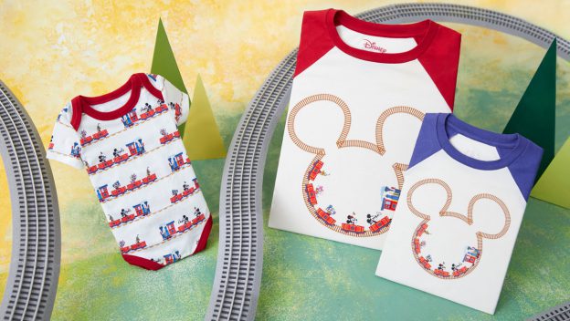A vibrant display features three Mickey Mouse-themed shirts adorned with charming train graphics, surrounded by playful toy train tracks on a colorful backdrop. Inspired by the whimsical atmosphere of Mickey & Minnie's Runaway Railway at Disney Parks, this setup is perfect for BoxLunch guests and Disney enthusiasts seeking magical merchandise from their favorite attraction.
