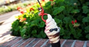 Mrs. Incredible Float-inspired soft serve, topped with superhero-themed decorations, served in a cup on a brick ledge surrounded by lush greenery at Disney Springs. This limited-time treat is perfect for fans visiting the park.