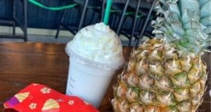 A refreshing Starbucks drink, a tropical pineapple, and a vibrant red face mask covered in playful Disney ice cream icons sit atop a wooden table—perfect for fans gearing up for a day at the parks.