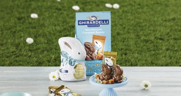 Ghirardelli’s Mini Caramel Bunnies and Milk Chocolate Bunny treats are artfully arranged on a table at Disney Springs, surrounded by lush grass and vibrant spring flowers, inviting guests to enjoy a sweet taste of Disney magic outdoors.