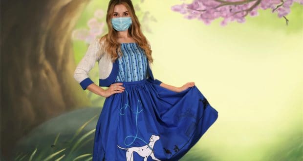 A Disney fan rocks a 101 Dalmatians dress and face mask in front of a dreamy pastel forest mural, capturing the playful spirit of Disney Springs.