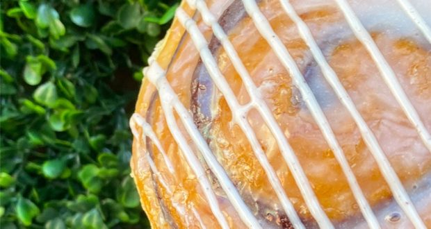 Everglazed Donuts’ famous cinnamon roll topped with sweet white icing, displayed beside lush greenery at Disney Springs.