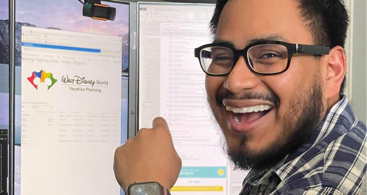 Excited Disney fan with glasses points at a computer screen displaying the Walt Disney World Vacation Planning page, spotlighting the popular Scheduler tool that Cast Members love for helping guests plan magical park adventures.