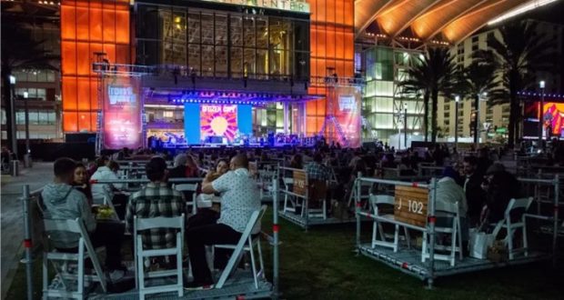Guests enjoy a Disney Broadway Concert under the stars at Dr. Phillips in Orlando, relaxing at safely spaced tables as the stage glows with vibrant lights and magical Disney music fills the night.