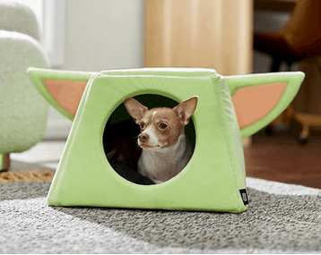 Adorable pup relaxing in a Yoda-inspired dog bed with iconic green ears, channeling Baby Yoda vibes on the galactic carpet at Star Wars: Galaxy's Edge.