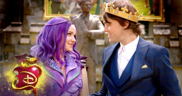 Mal and King Ben share a joyful moment, smiling at each other as they stand close during the enchanting Disney’s Descendants: The Royal Wedding celebration. The Disney Channel logo adds to the festive atmosphere, bringing fans right into the excitement of this magical event.