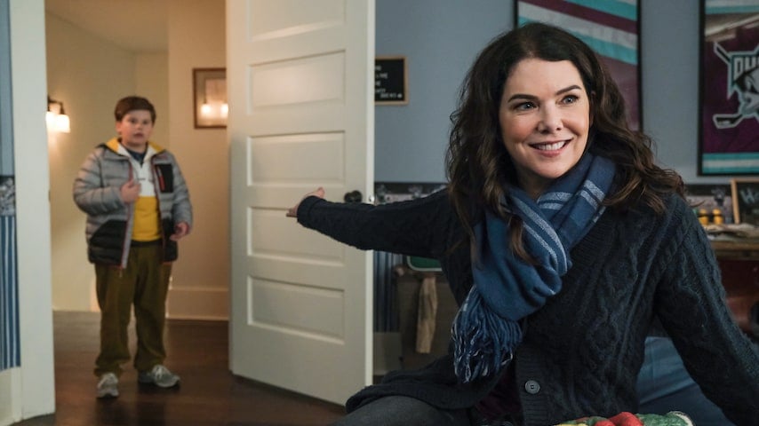 A cheerful woman greets a boy entering the room, both bundled up and sharing a joyful moment that captures the warmth and excitement fans love about Disney+ hits like The Mighty Ducks: Game Changers.