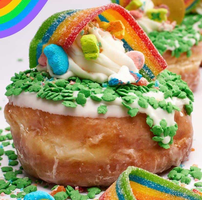 Experience the festive Shamrock Supreme Donut at Everglazed in Disney Springs—a glazed donut topped with white icing, vibrant green sprinkles, a rainbow candy strip, and colorful marshmallow bits for that perfect magical park treat.
