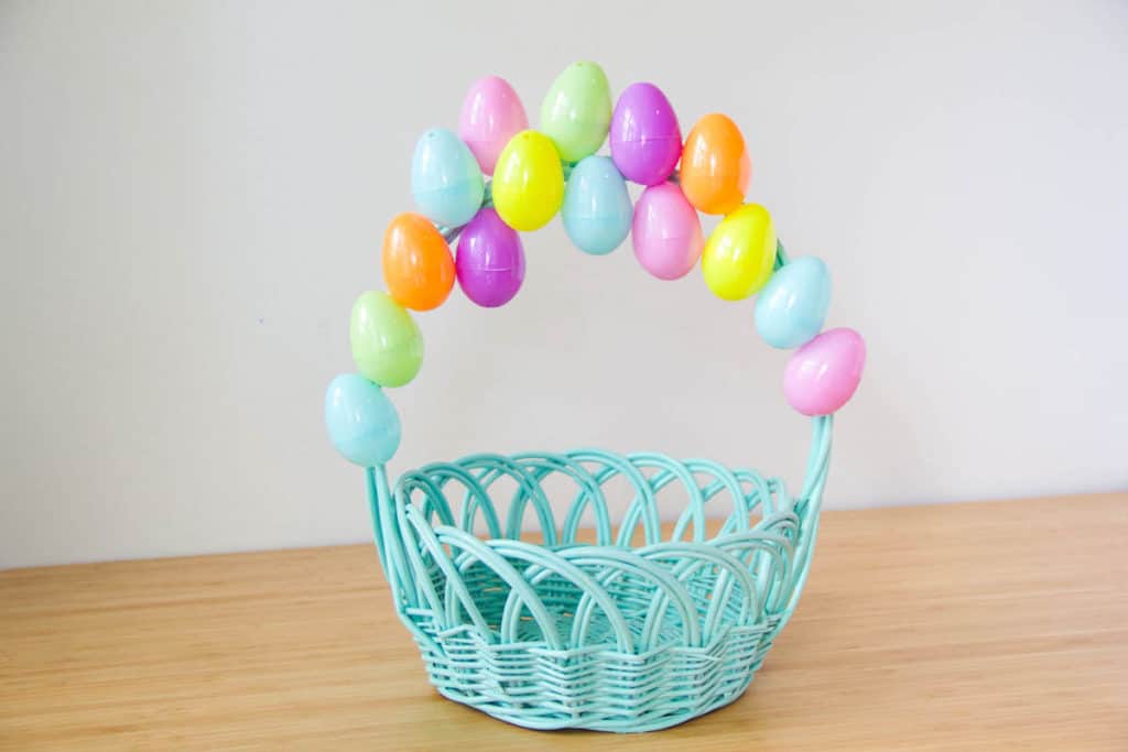 A blue wicker Easter basket, styled with colorful plastic eggs on its handle just like Carl’s iconic balloons, sits on a wooden surface—an eye-catching tribute to Pixar’s Up that would delight Disney Parks fans and movie lovers alike.