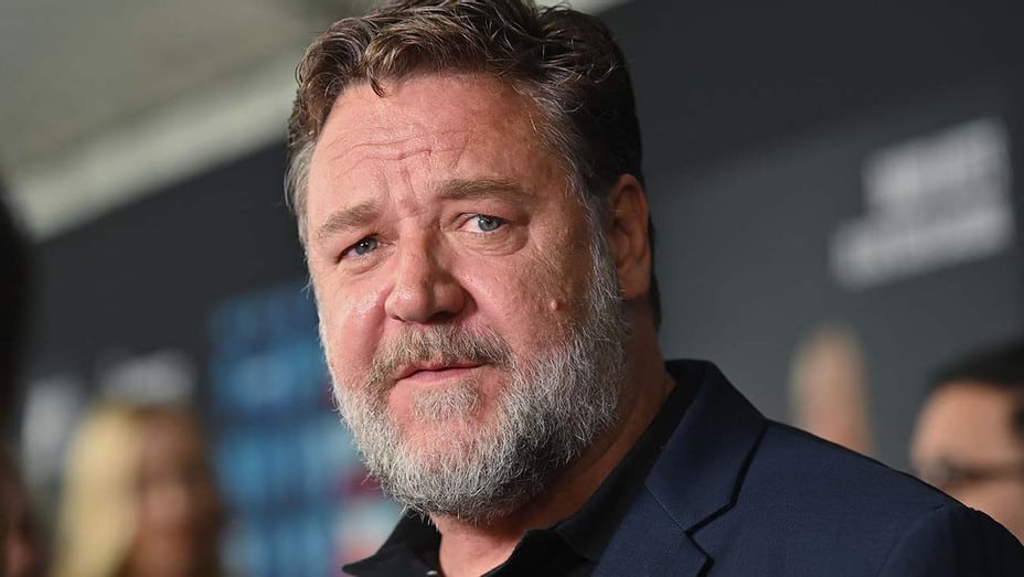 A Russell Crowe lookalike, sporting a dark jacket and bushy beard just like his role in Marvel’s Thor: Love and Thunder, greets guests with a friendly smile, set against the immersive themed backdrop.