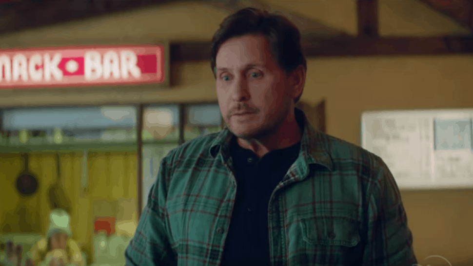 A guest dressed in a green plaid shirt pauses thoughtfully inside a Disney parks dining area, standing near a bright red snack bar sign, capturing the vibe of The Mighty Ducks: Game Changers.