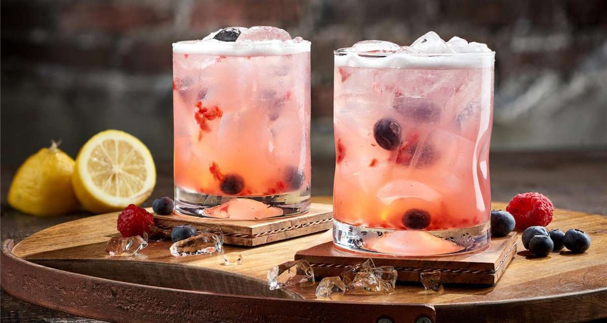 Berry Smash Cocktails from The Edison at Disney Springs, served in style with a layer of ice and foam, topped with blueberries and raspberries, ready to refresh you between adventures at Walt Disney World.