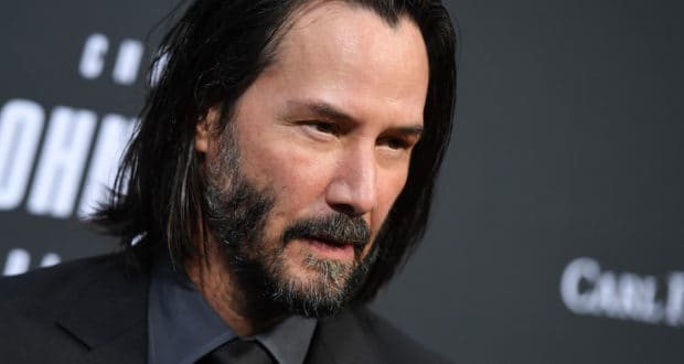Keanu Reeves lookalike with long dark hair and a beard, dressed in a sleek black suit, poses against a moody, cinematic backdrop—capturing the excitement for his rumored Star Wars role that has theme park fans buzzing about potential new attractions.