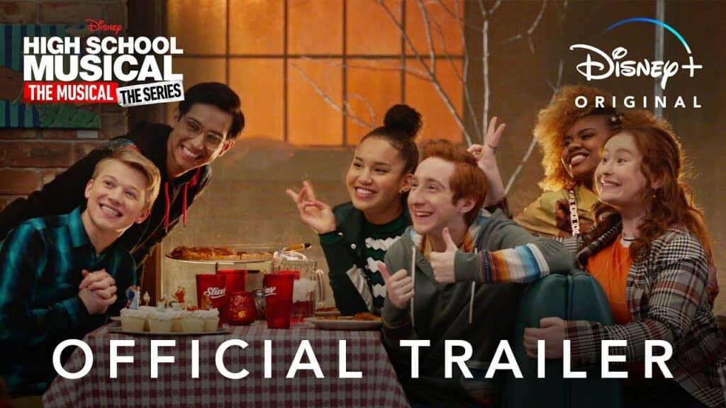 Cast members from High School Musical: The Musical: The Series Season 2 share a fun moment around a table topped with pizza and cake, smiling for the camera. The Disney+ and HSMTMTS logos highlight the excitement of this on-screen celebration.