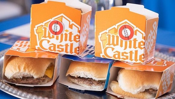 Four White Castle sliders served on a tray, with two signature orange and white boxes behind them—a delicious preview for foodies gearing up for White Castle’s grand opening next week at Walt Disney World.