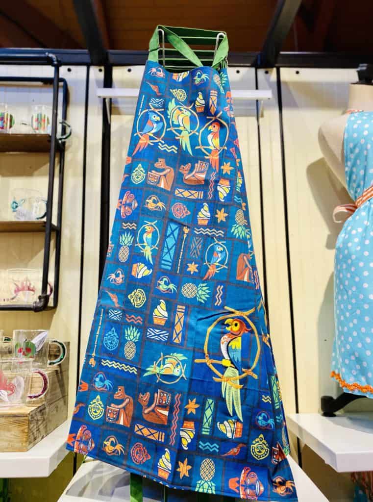 Brightly colored apron featuring tropical birds and bold geometric patterns is showcased in a well-lit store, capturing the lively, fun atmosphere and signature style of Disney Springs merchandise.
