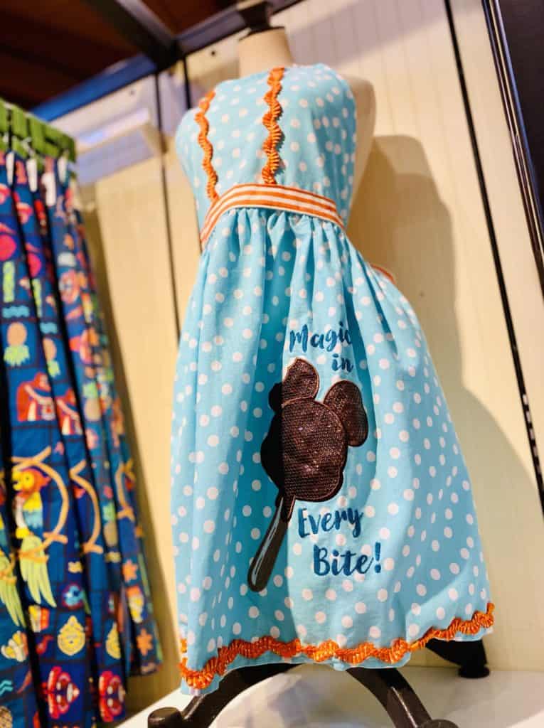 Step into Disney Springs style with this blue polka dot dress, featuring playful Mickey-shaped ice cream cones and the whimsical phrase "Magic in Every Bite!"—a must-have look for your next adventure at the parks or a magical day out.