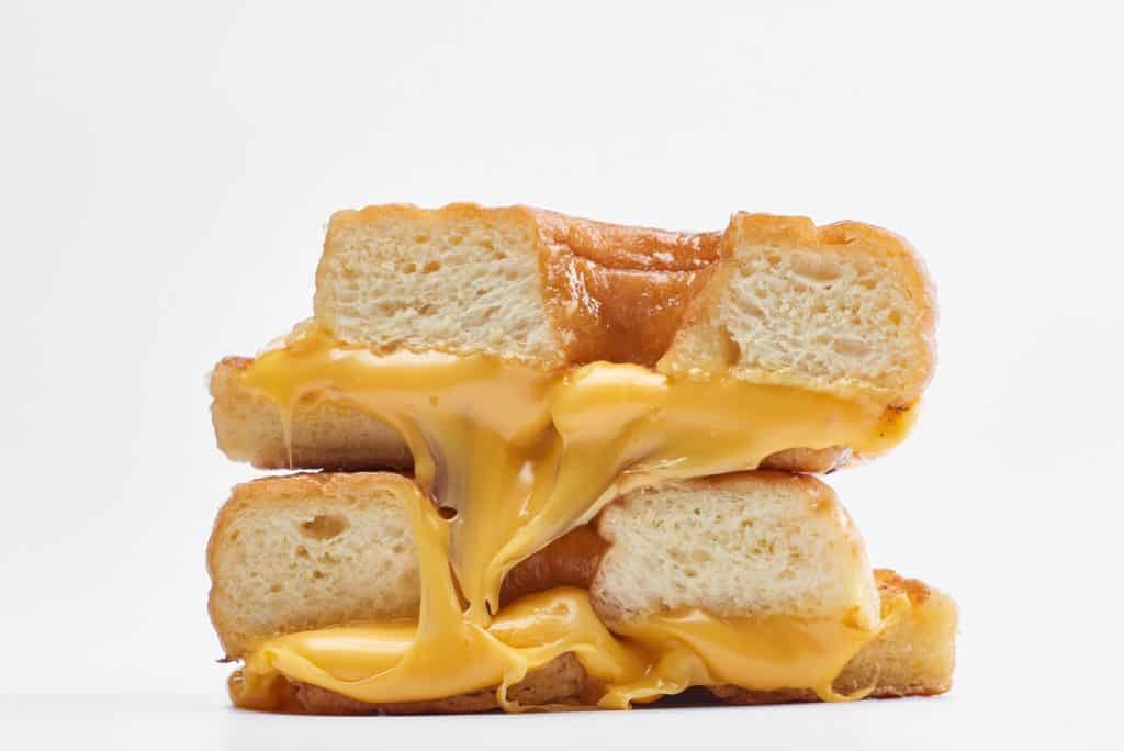 Golden grilled cheese sandwiches piled high, with gooey melted cheese spilling out just like the iconic Grilled Cheese Donut found at Disney Springs, all set on a simple white backdrop.