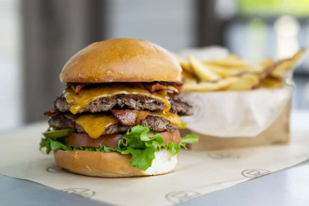 Introducing the Double Bacon Stack Burger at Disney Springs—a towering double cheeseburger piled high with crispy bacon, fresh lettuce, and tomato, served with golden fries on a tray. Perfect for fueling up between attractions in the heart of Disney magic!.