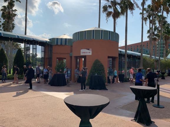 Guests line up outside the Swan and Dolphin’s check-in area, surrounded by palm trees and cocktail tables, enjoying sunny weather at Walt Disney World’s Spring Food & Wine Classic.