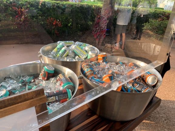At the Swan and Dolphin Spring Food & Wine Classic in Walt Disney World, three metal tubs packed with ice-cold canned drinks invite guests to grab a refreshment, while attendees mingle nearby under the sunny Florida sky.