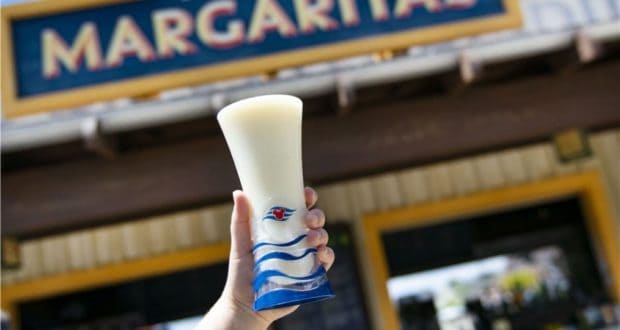 A refreshing frozen margarita in an Embarkation Glass is held up in front of a glowing "Margaritas" sign at Disney Springs, highlighting the energetic vibes and festive spirit of this popular Walt Disney World destination.