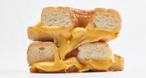Gooey melted cheese spills from a golden, sliced Grilled Cheese Donut sandwich, reminiscent of the over-the-top foodie favorites found at Disney Springs, set against a bright white backdrop perfect for fans eager to taste theme park magic.