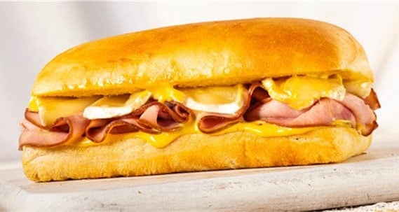 Le Frenchy sandwich with gooey melted cheese and savory ham slices on a perfectly toasted golden bun rests atop a white surface, capturing the mouthwatering flavors and Disney Springs magic that theme park foodies crave.