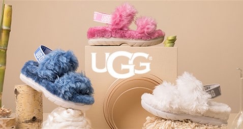 Three pairs of fluffy UGG sandals—in vibrant blue, pink, and classic white—are showcased with the UGG logo at the center, evoking a sense of fun comfort for exploring Disney Springs between thrilling attractions and magical shopping adventures.