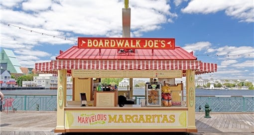 BoardWalk Joe's Marvelous Margaritas stand, bright yellow and freshly reopened, welcomes guests on the Disney boardwalk with waterfront views under a sunny blue sky.